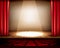 A theater stage with a red curtain, seats and a spotlight.