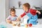 TheLittle girl kneads dough on kitchen table at home with delight. Her younger brother is sitting on the table and estimates for