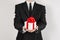 Theme holidays and gifts: a man in a black suit holds an exclusive gift in a white box wrapped with red ribbon and bow isolated on