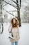 Theme is weekend holiday in winter. A beautiful young Caucasian woman stands in a snow covered park in jacket with hood and fur in