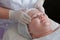 Therapeutic and cosmetological facial massage of a fat woman. The hands of a professional beautician in white medical gloves