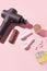 Therapeutic percussive massage gun, fit meal, pills, sport energy bar on pink background - concept of modern sport activity and