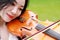 There is a Asian Eastern Chinese young beautiful pretty artist woman play violin by river in a park garden forest. she is in white