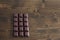 There is a bar of dark chocolate on the wooden table