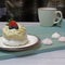 There is a blue wooden tray on the table. On the saucer is a white meringue cake with cream