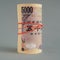 There is a bundle of 5,000 yen Japanese bills close-up. Dark gray backdrop. The banknotes are rolled up and tied with an elastic