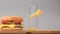 There is a burger and an empty glass on the table. Slices of fries are falling