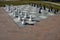 There is a chess area on square with lawn around. chess pieces are made of plastic. The playing area is large tiled with black and