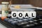 There are cubes on the calculator that say - GOAL. Nearby out of focus - dollars, notebook and pen