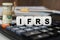 There are cubes on the calculator that say - IFRS. Nearby out of focus - dollars, notebook and pen