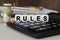 There are cubes on the calculator that say - RULES. Nearby out of focus - dollars  notebook and pen