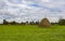 There is a haystack in the meadow, against the background of abandoned dilapidated wooden houses.