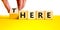 There or here symbol. Businessman turns a wooden cube, changes the word `there` to `here`. Beautiful yellow table, white