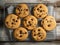 There are nine chocolate chip cookies on baking sheet, arranged in two rows. The cookies have been freshly made and