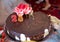 There are red flowers and rings on it . A dark chocolate tort . Round chocolate cake. 25 year old candle .