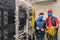 There are two technicians in medical masks in the server room. Specialists with a coil of wires in their hands work near the racks