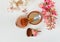 There White and Pink Branches of Chestnut Tree,Bronze Powder with Mirror and Two Make Up Brushes are on White Table,Top View