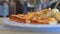 There is a white plate with a cut pie or pizza on the table in the restaurant, people pass by, selective focus, blur. Breakfast or