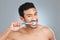 Theres a right way to brush and floss your teeth. a man brushing his teeth while standing against a grey background.