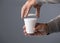 Thermal cup, man`s hands putting lid on recyclable container, gray background