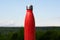 Thermo stainless bottle, sprayed with water. Sky and forest on background. Thermos of matte red color.