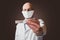 Thermometer in doctor`s hand in focus, bald male doctor in white uniform and mask out of focus, selective focus, Brown background