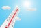 Thermometer with high temperature against the sun on blue sky background