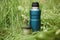 Thermos and mug standing on the grass outdoors. Steam rising from a steel mug of hot tea. Vacuum travel flask