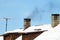 Thick and black smoke comes out of the chimney of an old private house.