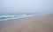 Thick, dense fog over the ocean as waves break on the empty beach.