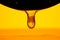 Thick drops of honey flowing down from a dark black spoon on yellow background. Golden streams of honey molasses or