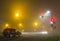Thick fog over empty road with lonely car and traffic lights at