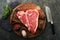 Thick Raw T-Bone Steak. Dry-aged Raw T-bone or porterhouse beef meat Steak on cutting boar with herbs and salt on dark