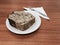 Thick slice of cake with chocolate topping on a white plate on a wooden table