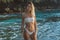 Thin girl in white swimsuit stands in the water on the bushy tropical beach,