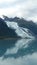 Thin Glacier between two mountains slowly gliding into the pacific ocean with a cloudy backdrop