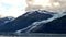 Thin Glacier between two mountains slowly gliding into the pacific ocean with a cloudy backdrop