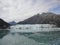 Thin Glacier between two mountains slowly gliding into the pacific ocean with a cloudy backdrop