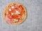 Thin pizza with high meat content. Uncooked product with cheese, salami, ham and tomato sous on simple grey table cloth. Dinner