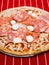 Thin pizza portion with high meat content. Uncooked product with cheese, salami, ham and tomato sous on simple grey red and white