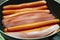 Thin sausages cut lengthwise are fried on a scoop. A lot of them lie in a row.