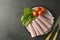 Thin slices of ham rolled on plate with fresh vegetables, dark background. Breakfast food, ingredient for sandwich. Flat lay food