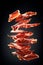 Thin slices of Spanish jamon flying in the air on black background. Traditional meat specialty of the local cuisine