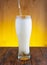 a thin trickle of light beer flows into a glass glass, beer with a thick rising white foam. wooden background.