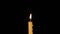 Thin wax candle burning on a black background. Close-up.