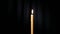 Thin wax candle burning on a black background with white beam