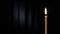 Thin wax candle burning on a black background with white beam