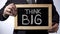 Think big written on blackboard, male in suit holding sign, motivational concept