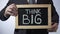 Think big written on blackboard, male in suit holding sign, motivational concept