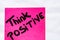 Think positive handwriting text close up isolated on pink paper with copy space. Writing text on memo post reminder